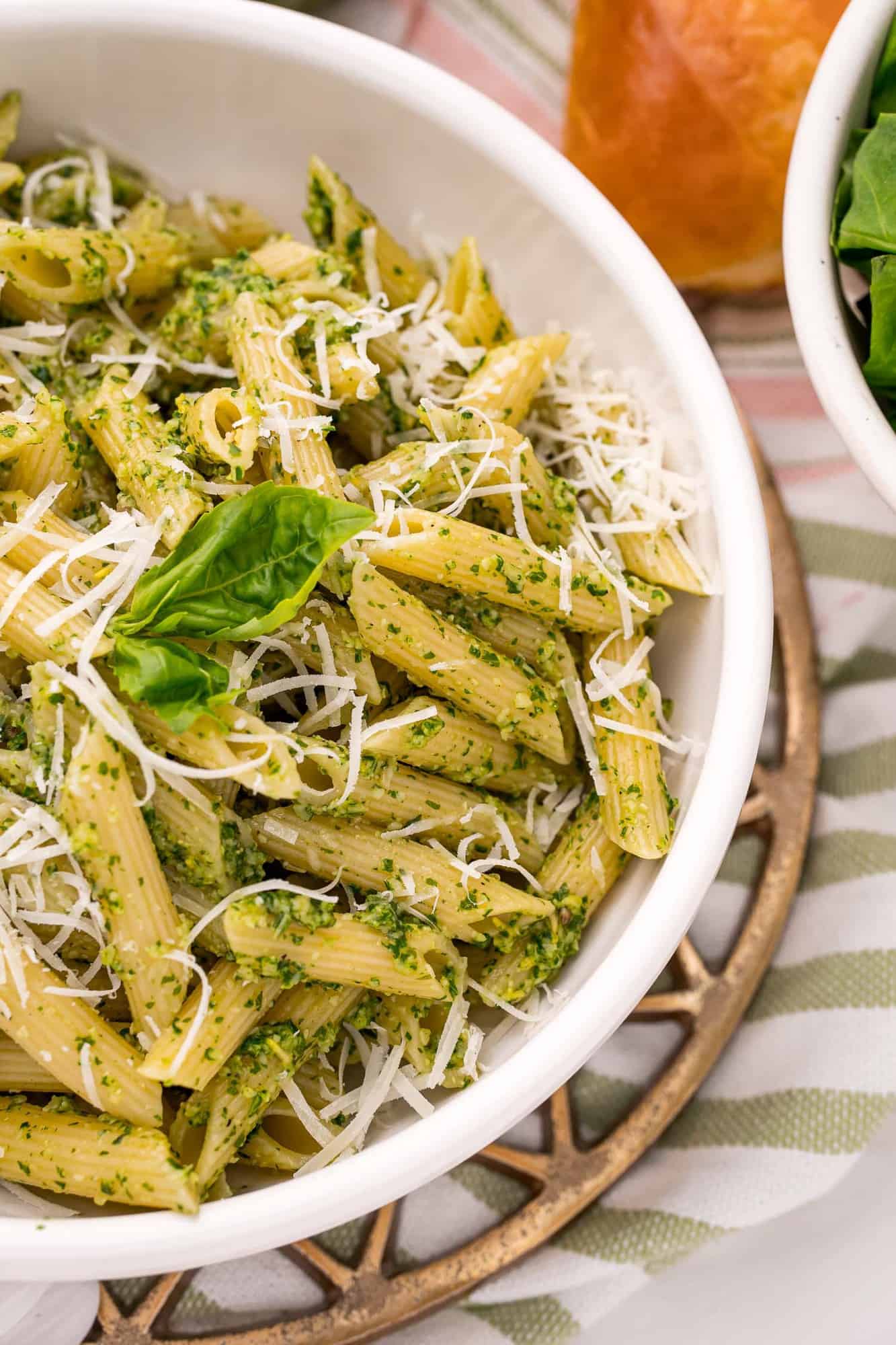 Penne pasta in a white bowl coated with pesto.