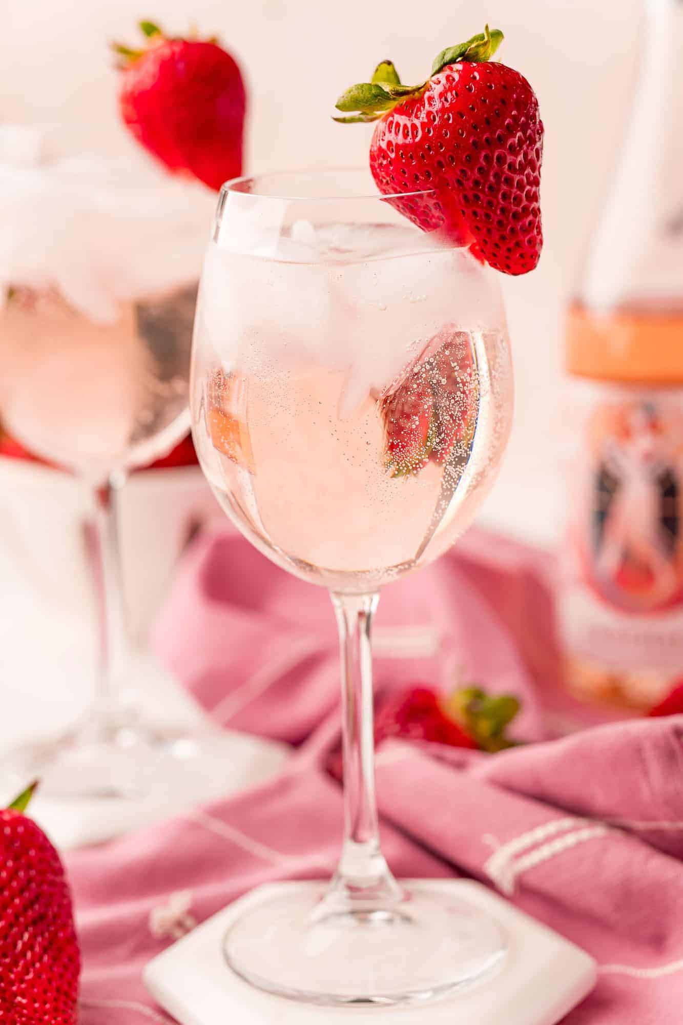 Close up of a wine glass with a rose spritzer, ice, and strawberry garnish.