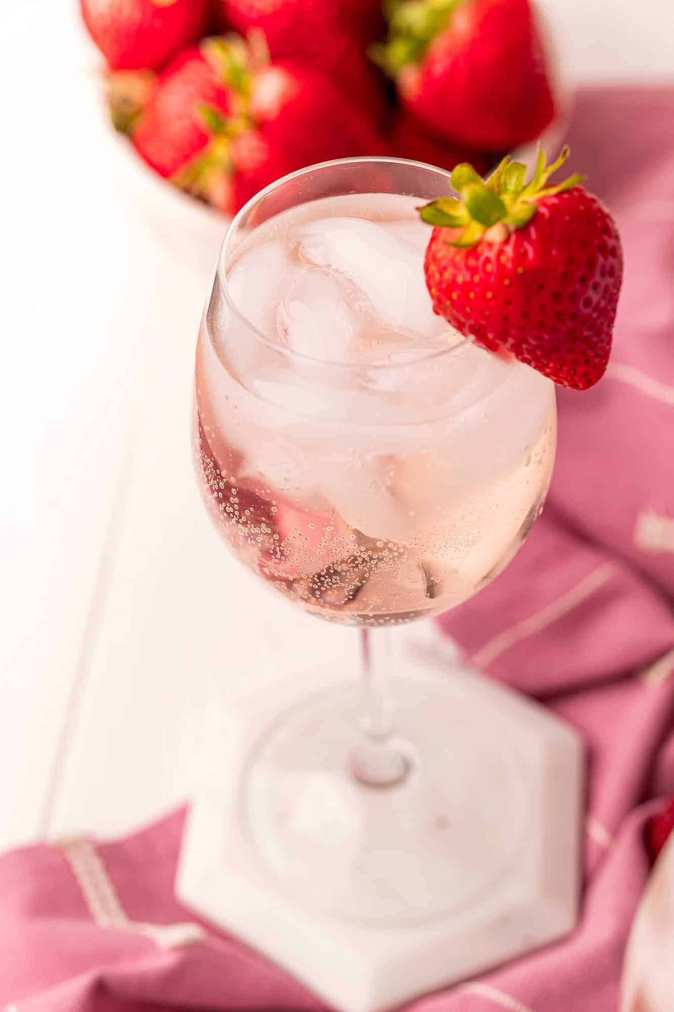 Light pink iced drink in a stemmed wine glass with a strawberry garnish.