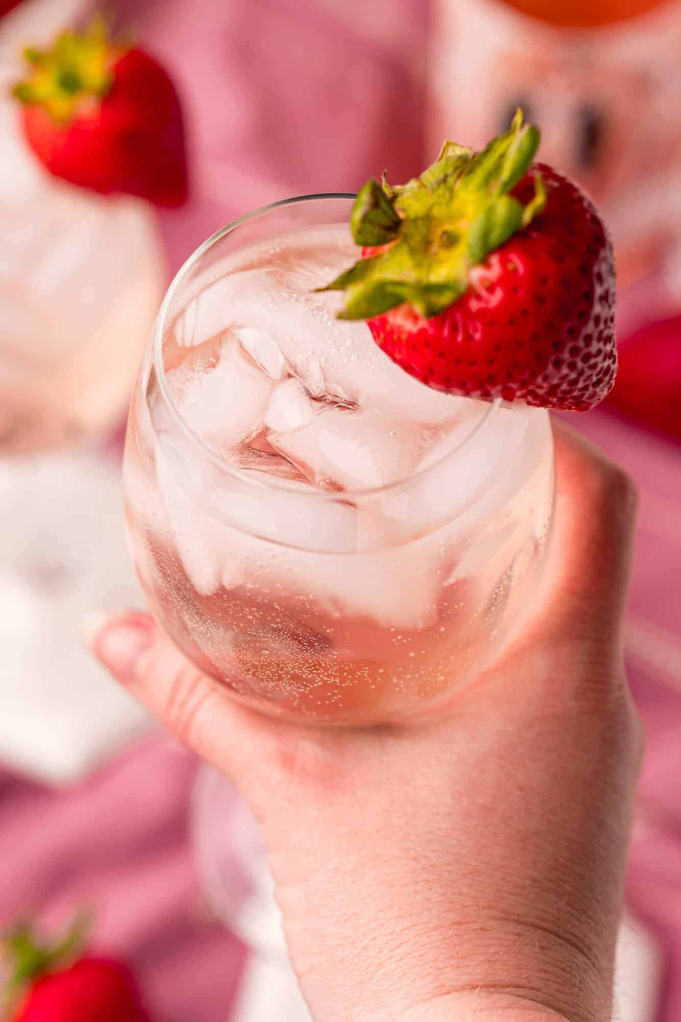 Iced cocktail with strawberry garnish in a person's hand.