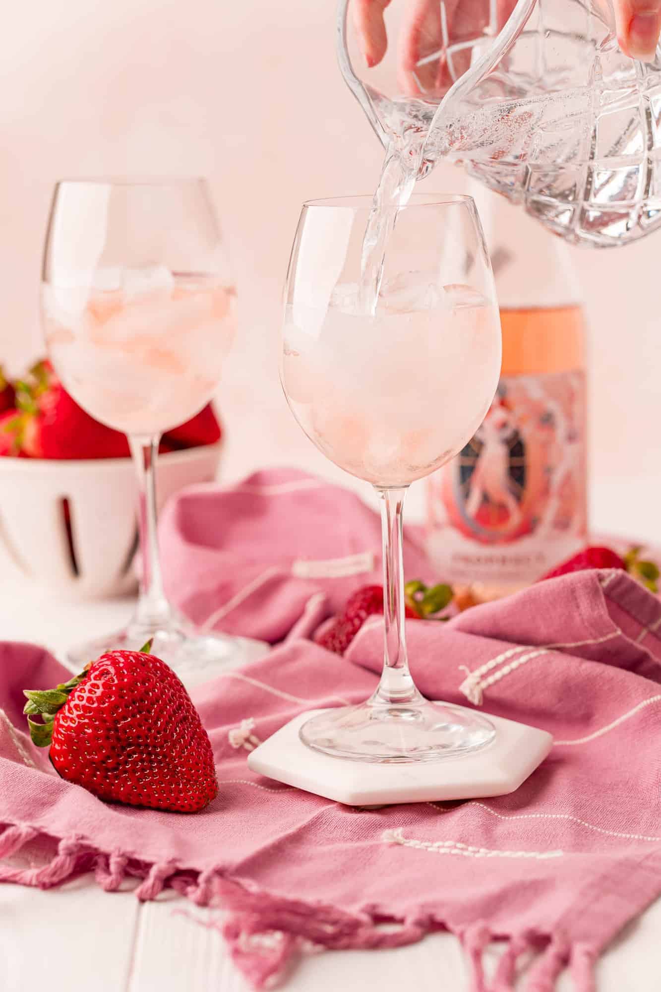 Club soda being poured into a wine glass with ice and rose wine.