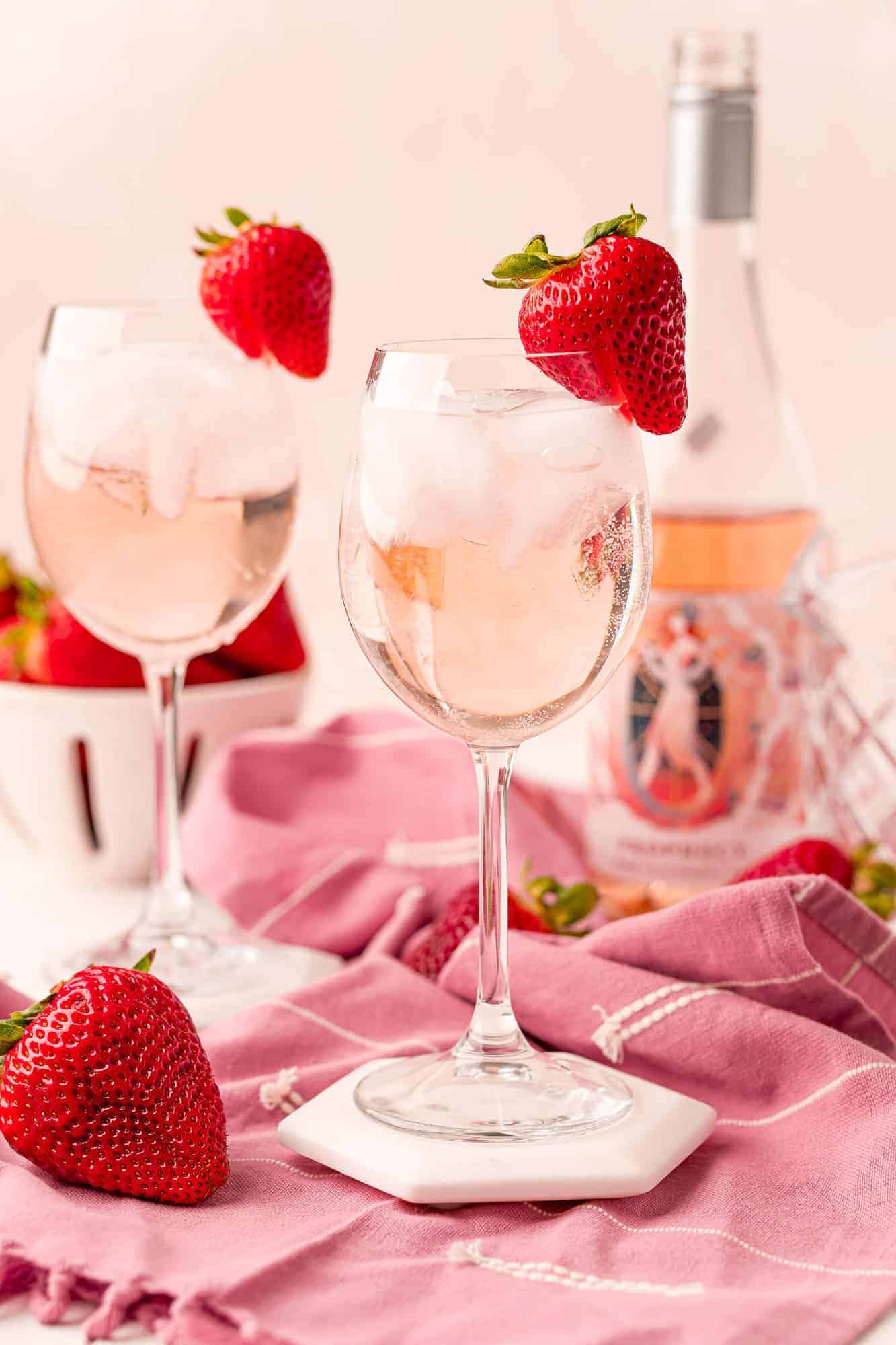 Two stemmed glasses with iced rosé spritzers, garnished with strawberries.