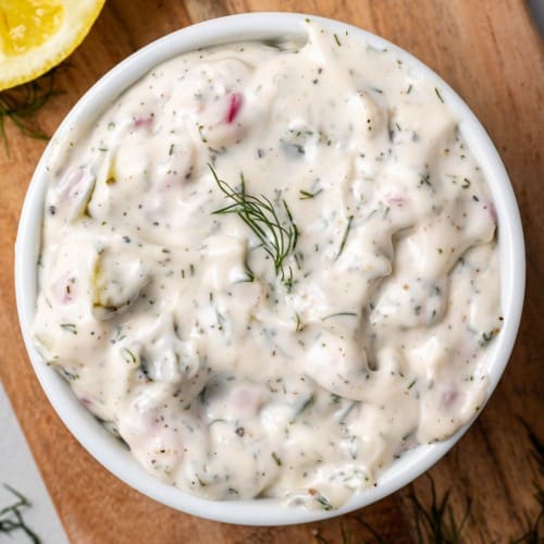 Overhead view of tartar sauce in a round white bowl garnished with fresh dill.