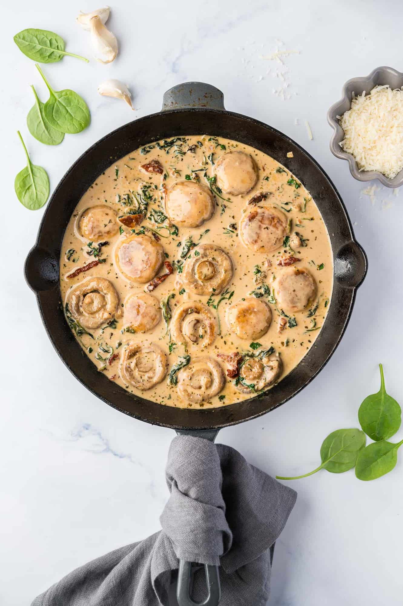 Overhead view of creamy tuscan mushrooms in a black skillet. Basil leaves are sprinkled around.