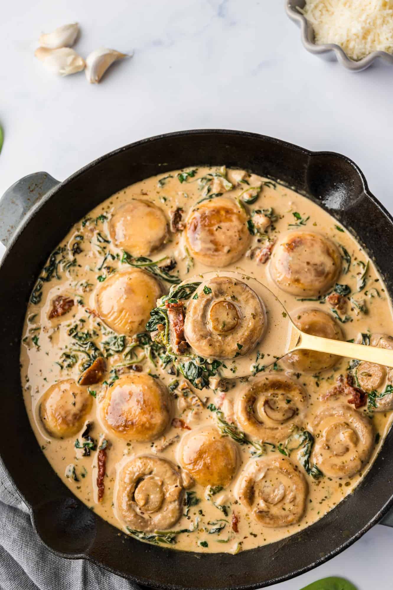 Overhead view of a black skillet filled with tuscan mushrooms with spinach and sun dried tomatoes.