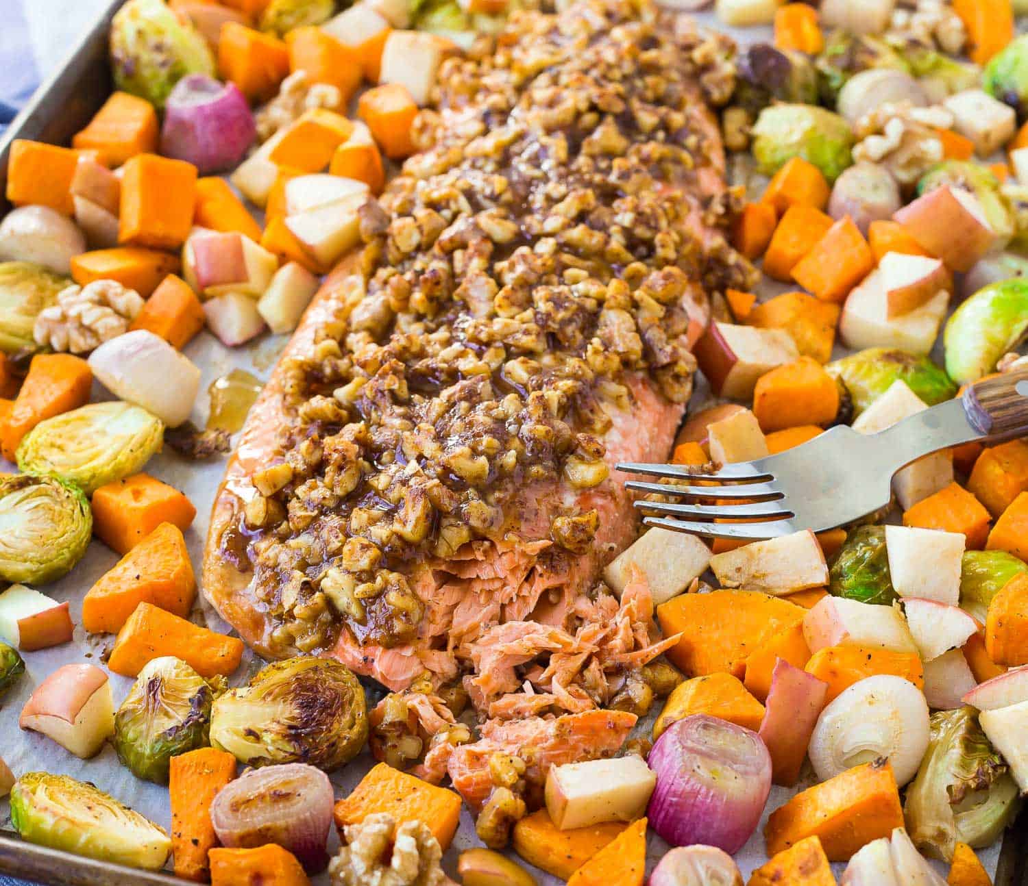 Salmon on a sheet pan, flaked to show texture. Vegetables surround meat.