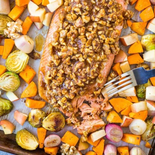 Overhead view of walnut crusted salmon on a sheet pan with vegetables, a fork is flaking salmon.