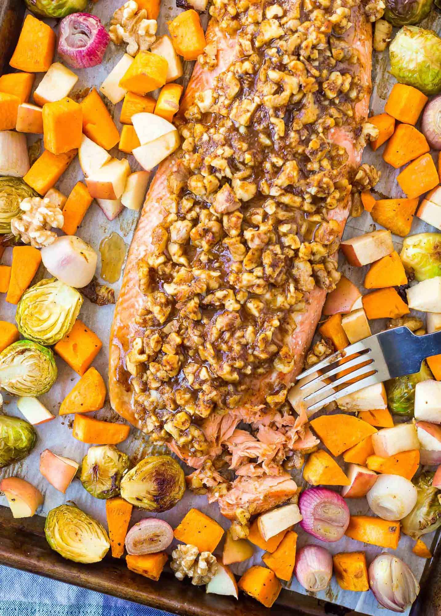 Overhead view of walnut crusted salmon on a sheet pan with vegetables, a fork is flaking salmon.