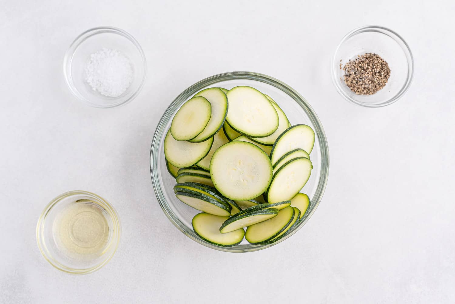 Overhead view of ingredients needed to make recipe: sliced zucchini, salt, pepper, oil.