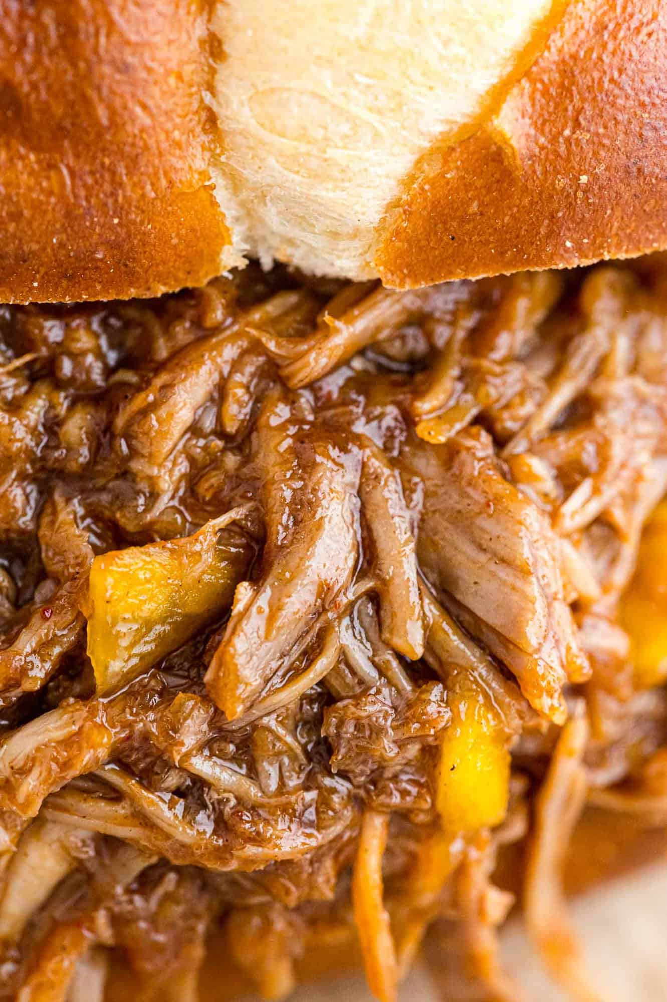 Very close up view of pulled pork with mango, on a bun.