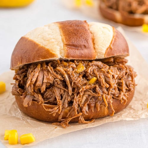 Pulled pork on a pretzel bun on natural colored parchment paper.