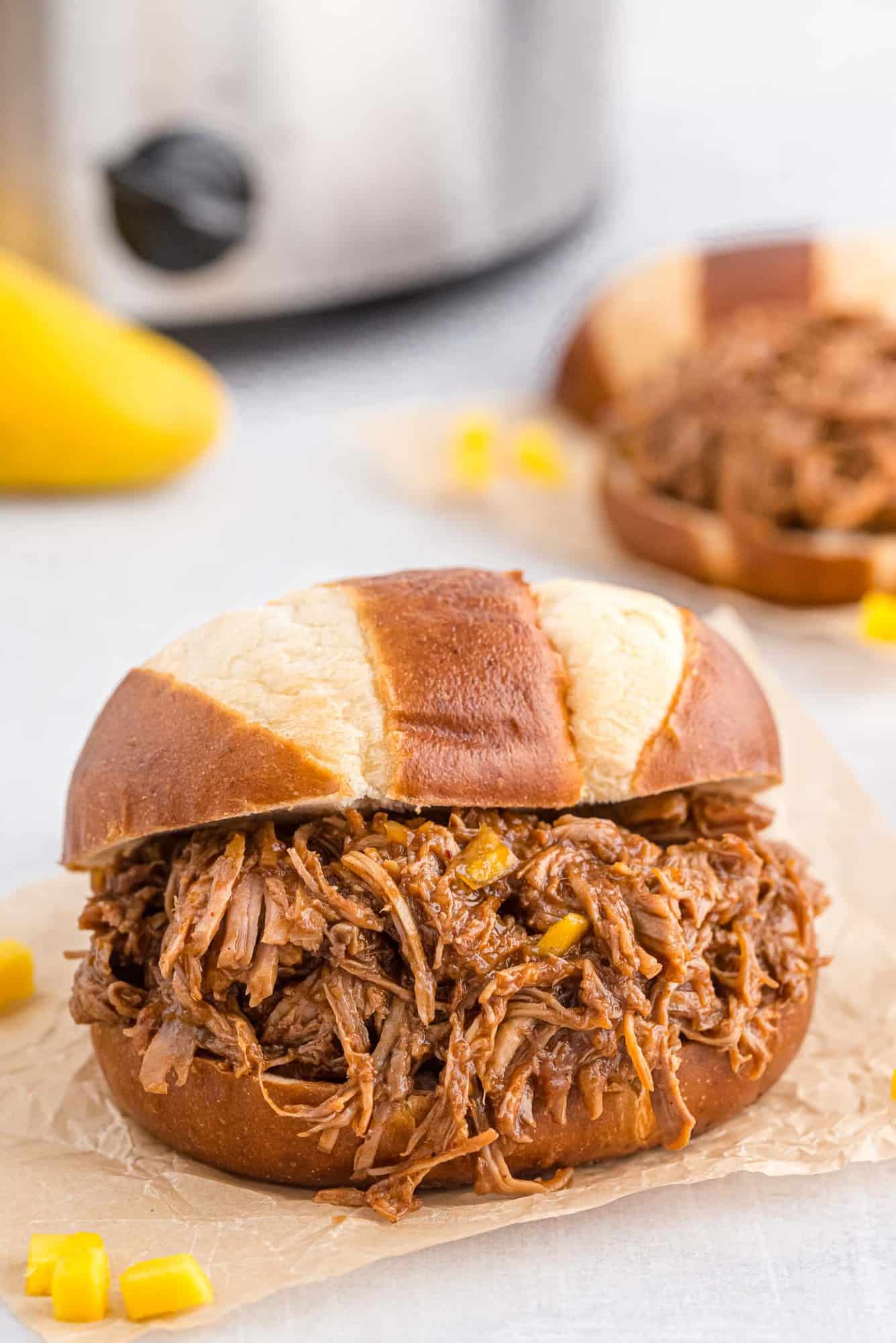 Pretzel bun piled high with pulled pork, a slow cooker pictured in the background.