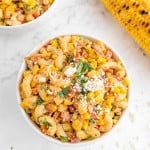 Overhead view of round bowl of pasta salad with macaroni, corn, red peppers, cotija, and cilantro.
