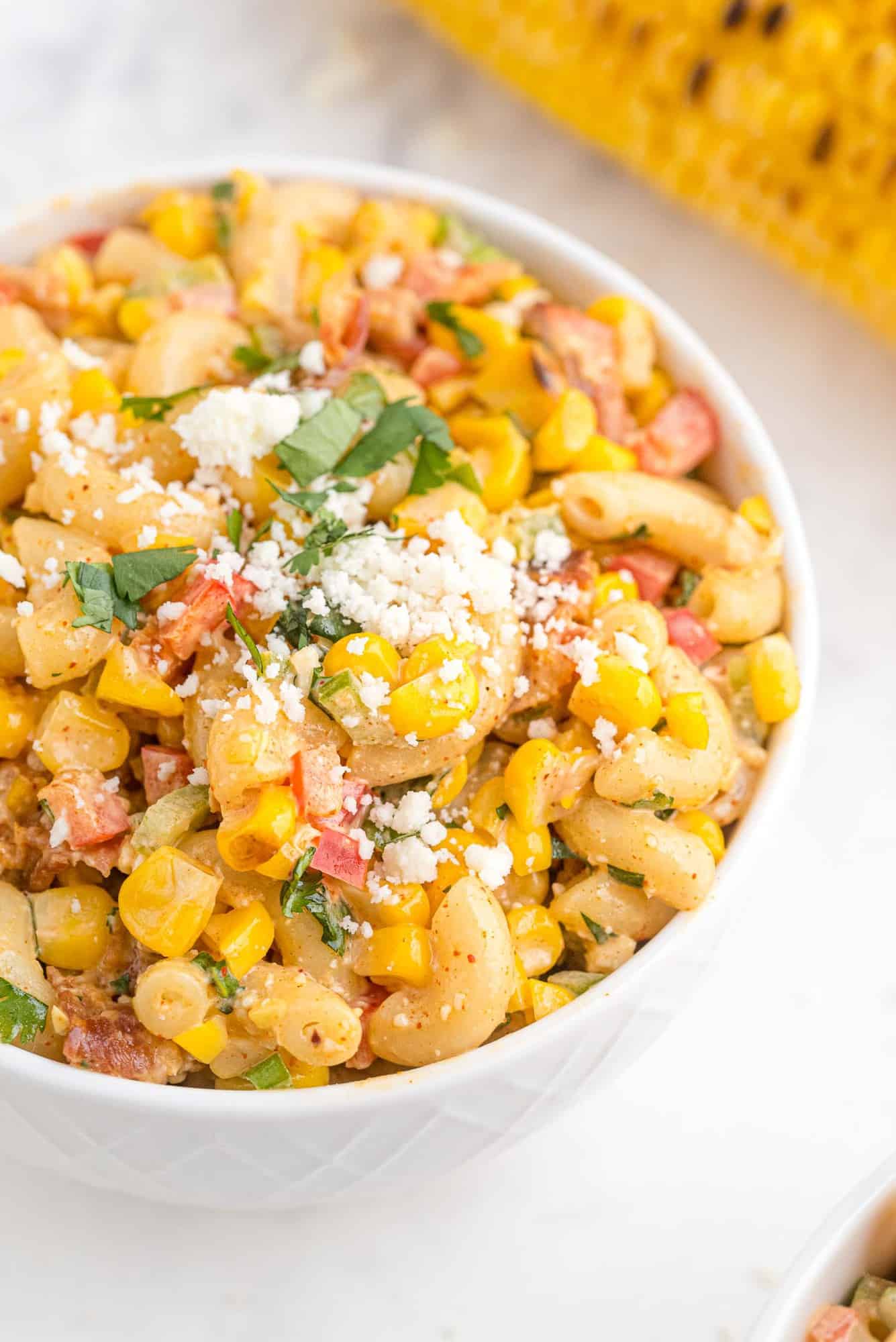 Pasta salad with corn and cheese in a round white bowl.