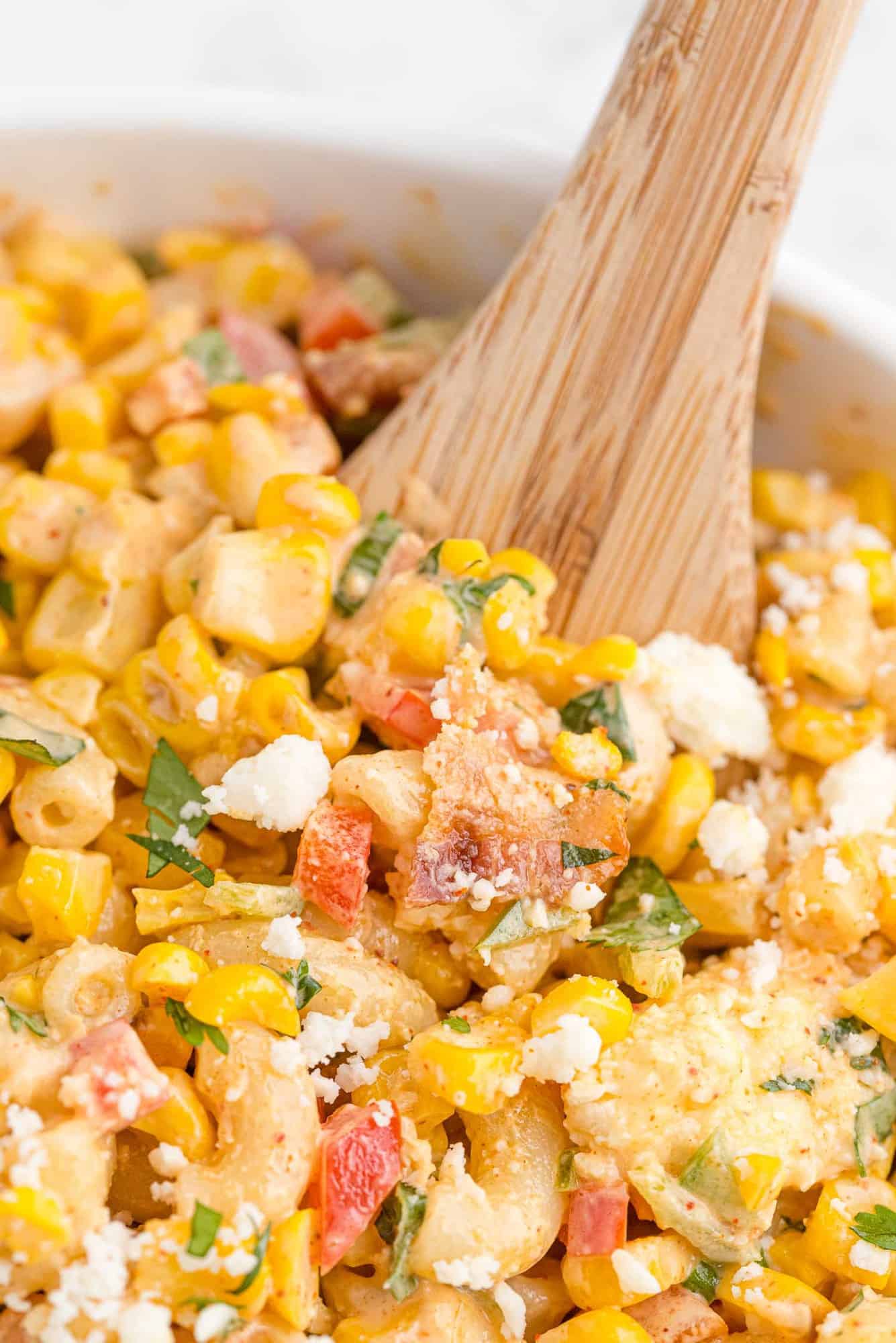 Close up of corn pasta salad with a wooden spoon in it.