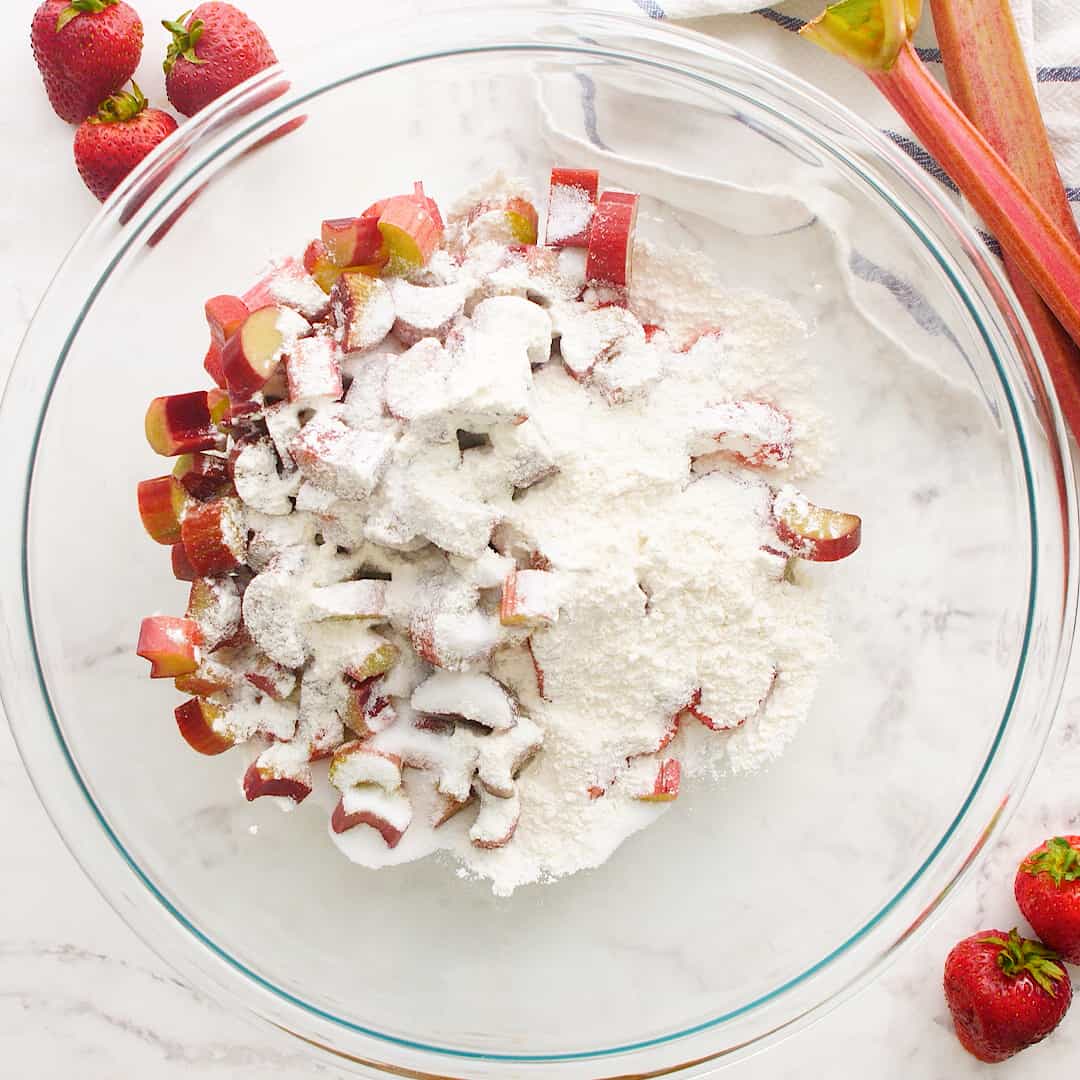 Rhubarb and strawberries in a glass bowl with flour mixture on top.