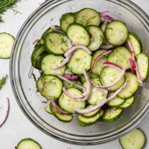 Overhead view of sliced cucumbers and onions in a clear glass bowl.