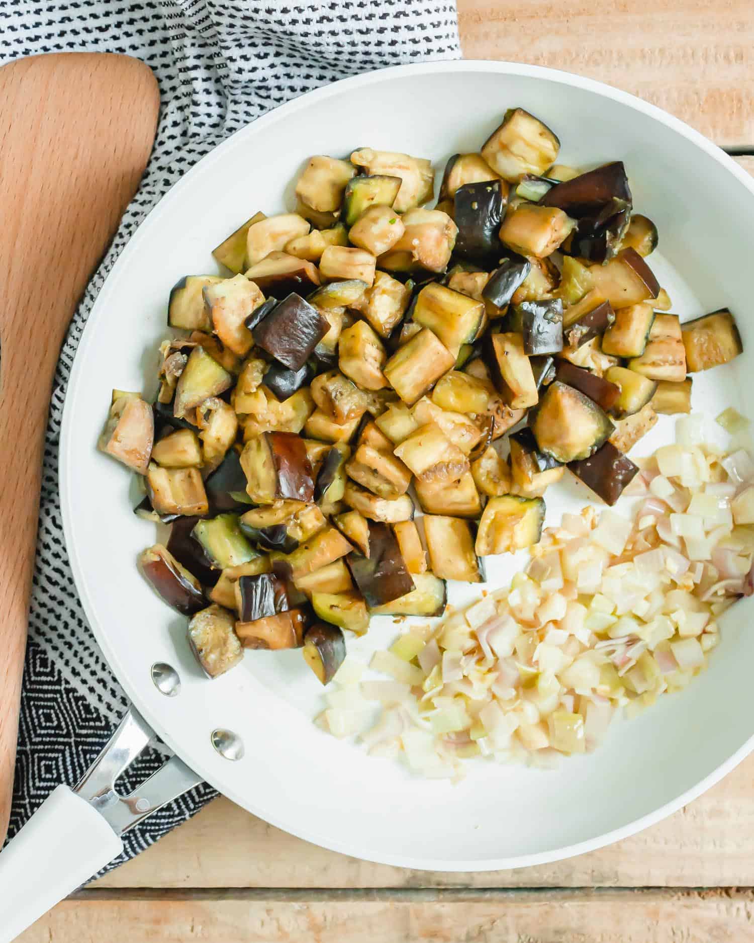 Eggplant and onions in a white frying pan.