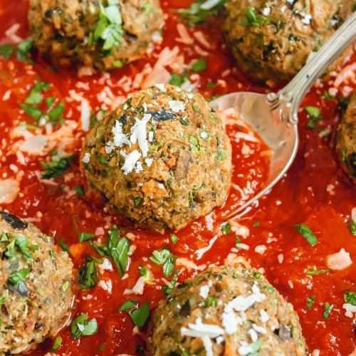 Eggplant vegetarian meatballs in a red sauce, one on a spoon.
