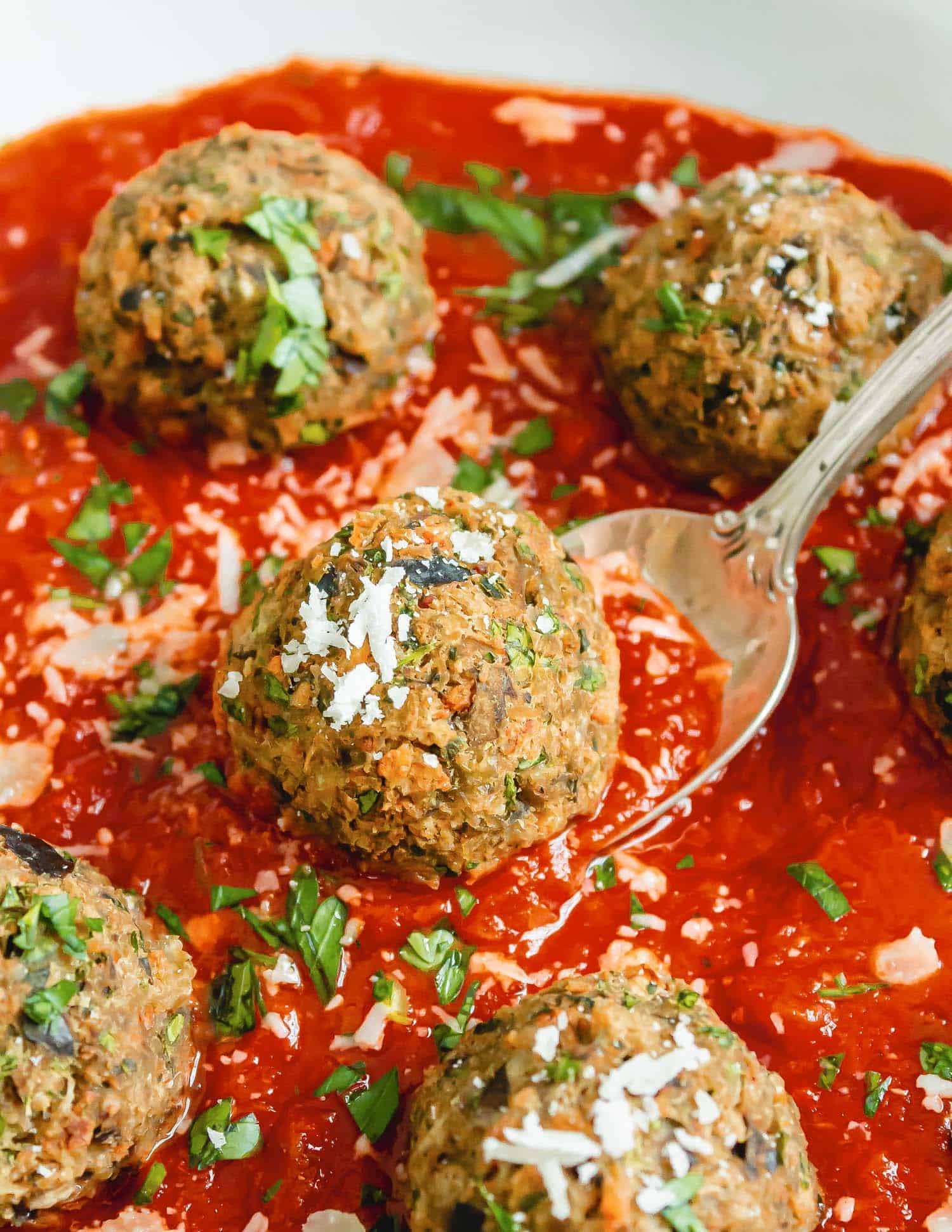 Close up of an eggplant meatball on a spoon, in sauce.