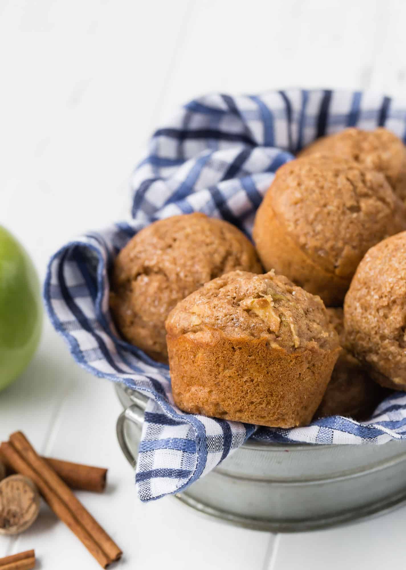 Whole wheat apple muffins in a metal basket with a blue and white checkered towel.