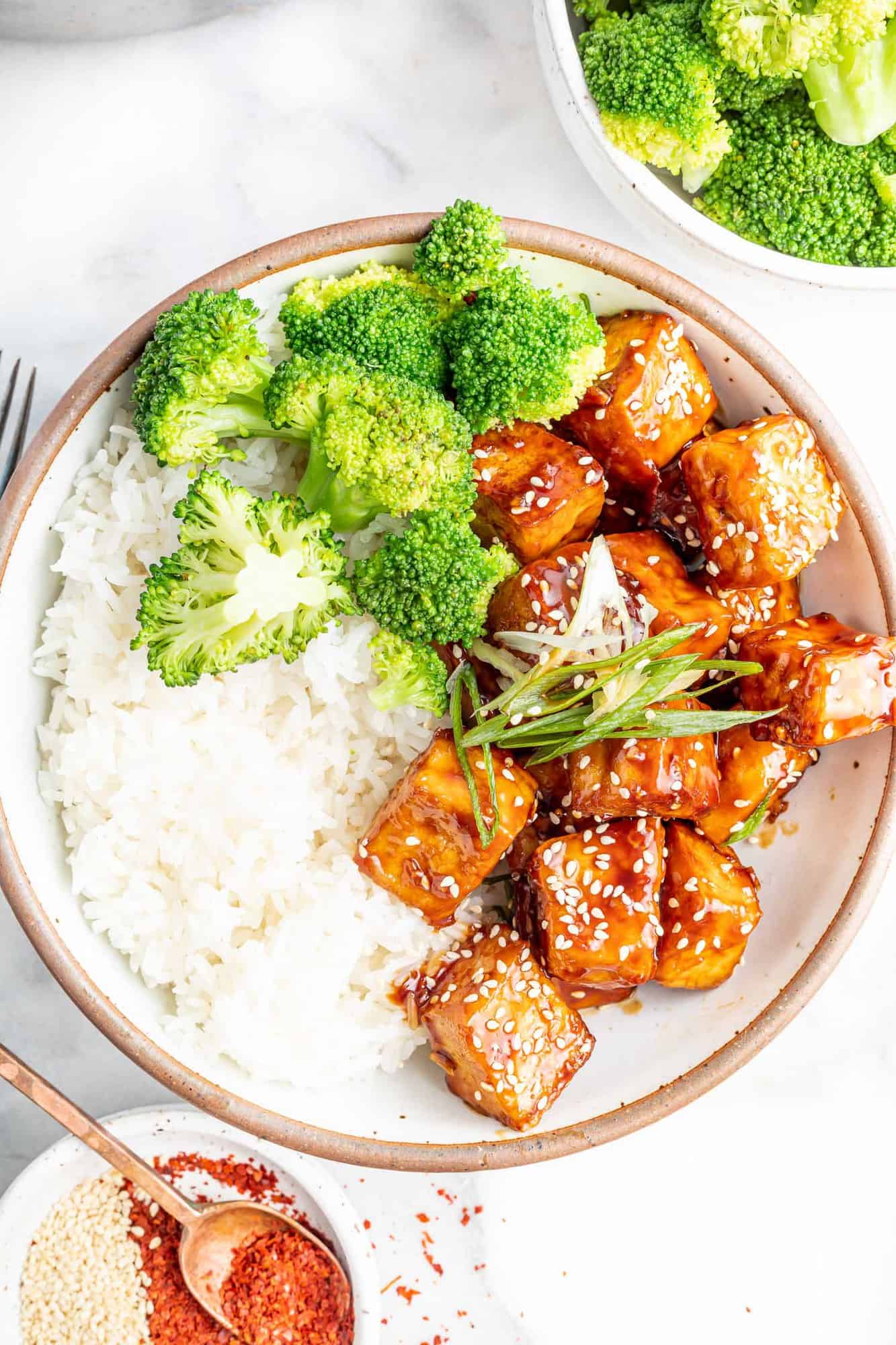 Overhead view of tofu in a bowl with rice and broccoli.