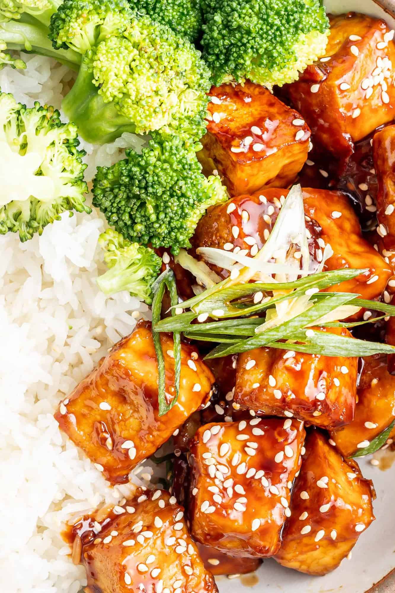 Close up of tofu served with rice and broccoli, sprinkled with sesame.