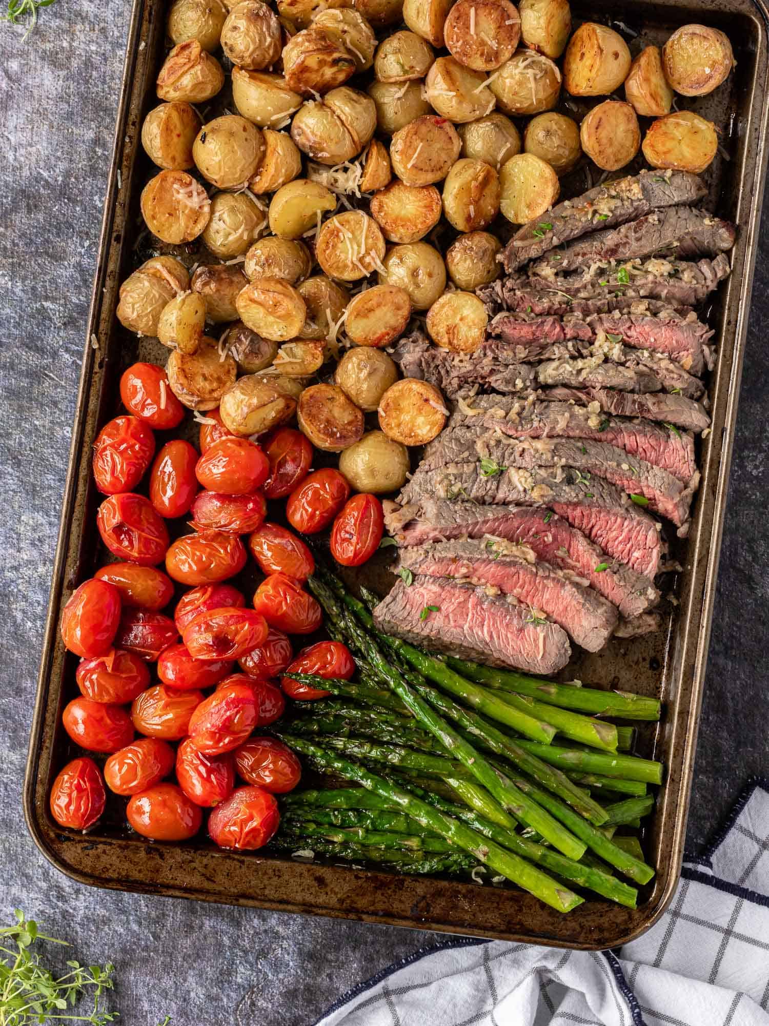 Cut steak, pink inside, on a sheet pan with tomatoes, potatoes, asparagus.