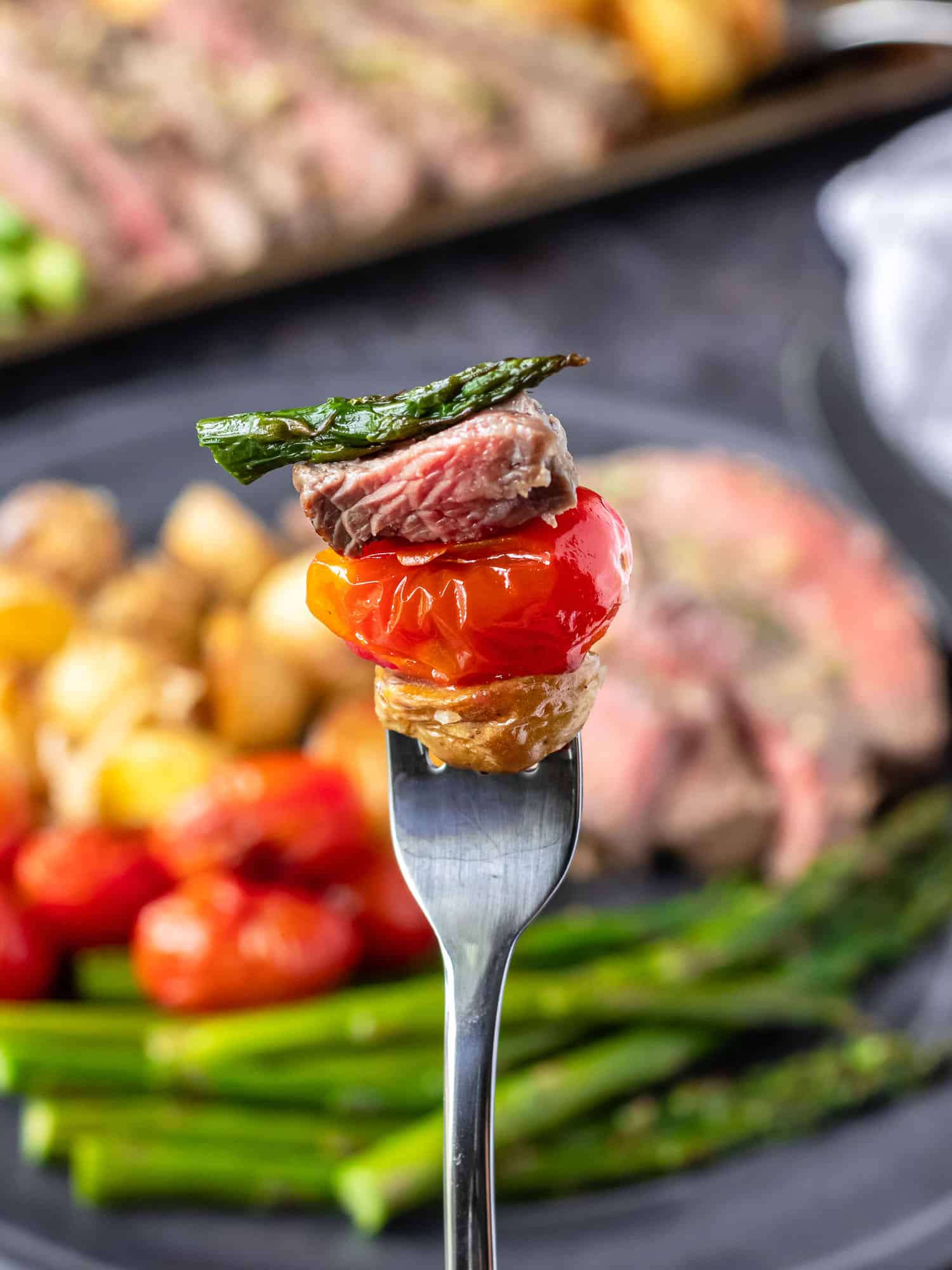 Steak on a fork with a tomato, potato, and asparagus.