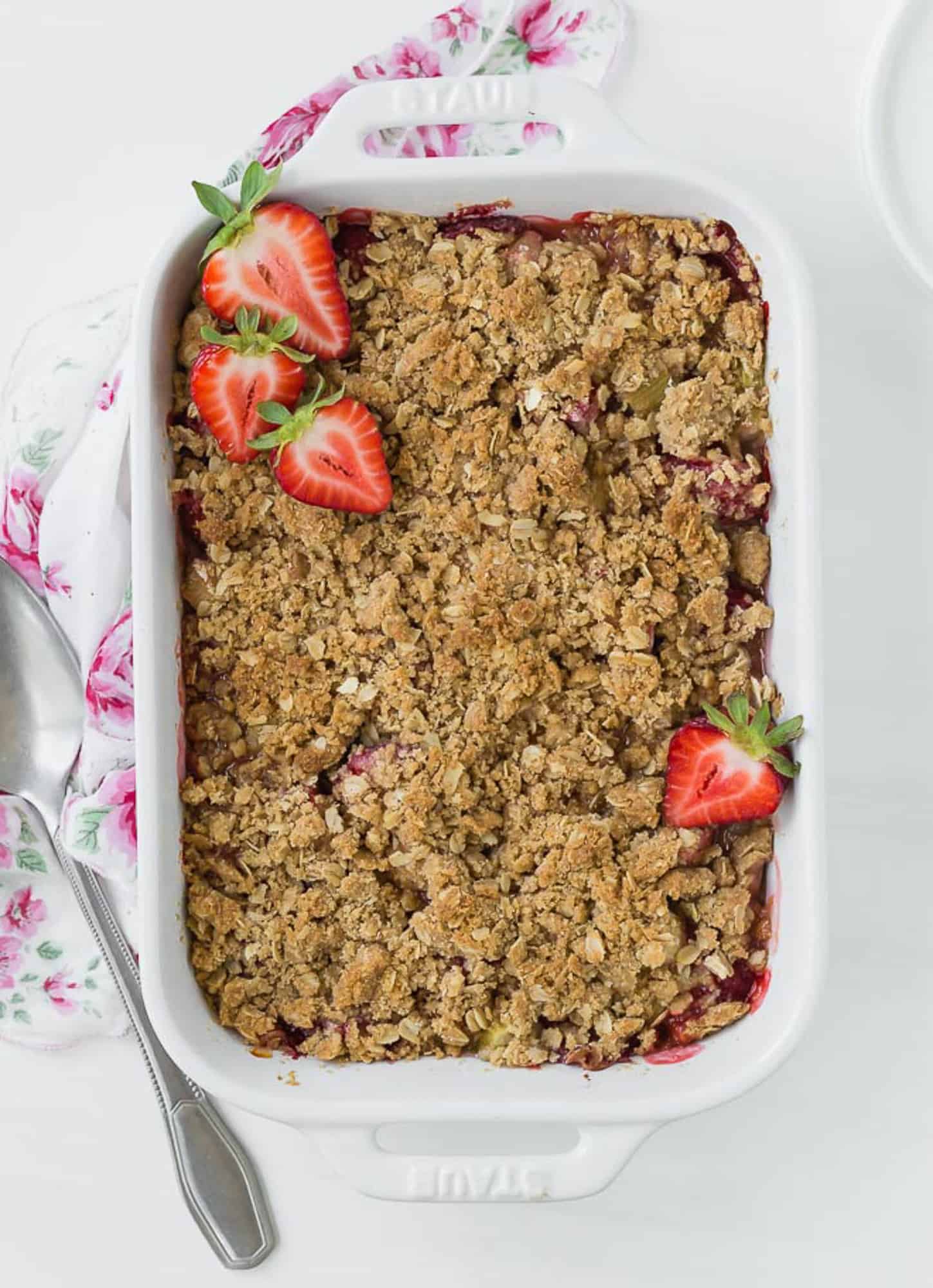 Overhead view of a white baking dish full of cooked strawberries and rhubarb, topped with fresh strawberry halves.