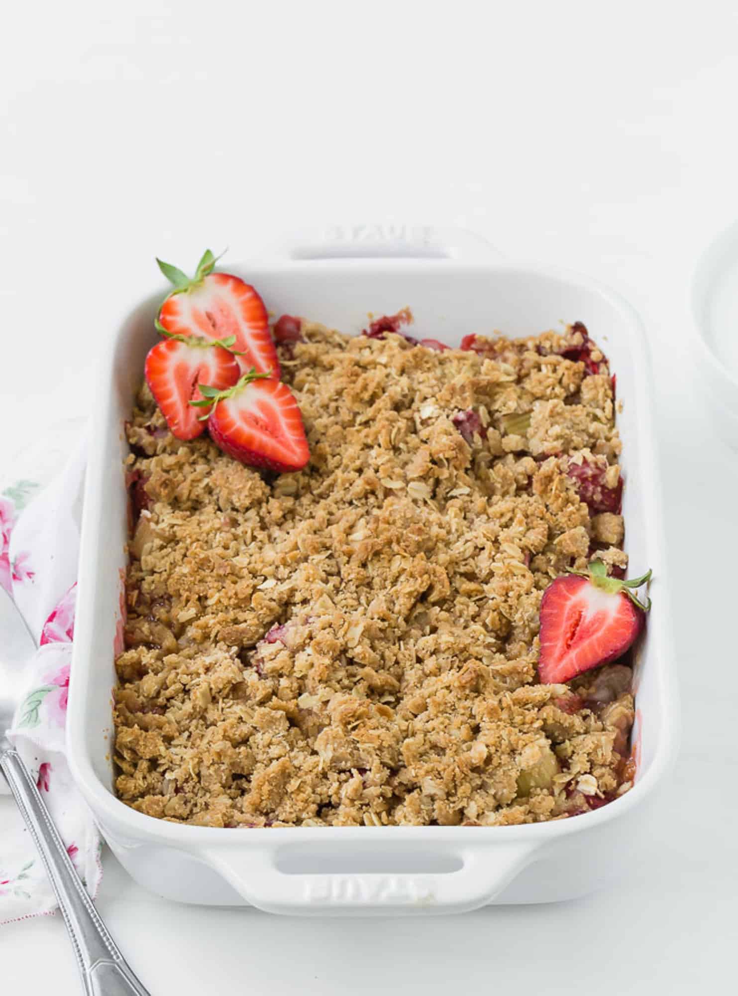 White baking dish full of cooked strawberries and rhubarb, topped with fresh strawberry halves.