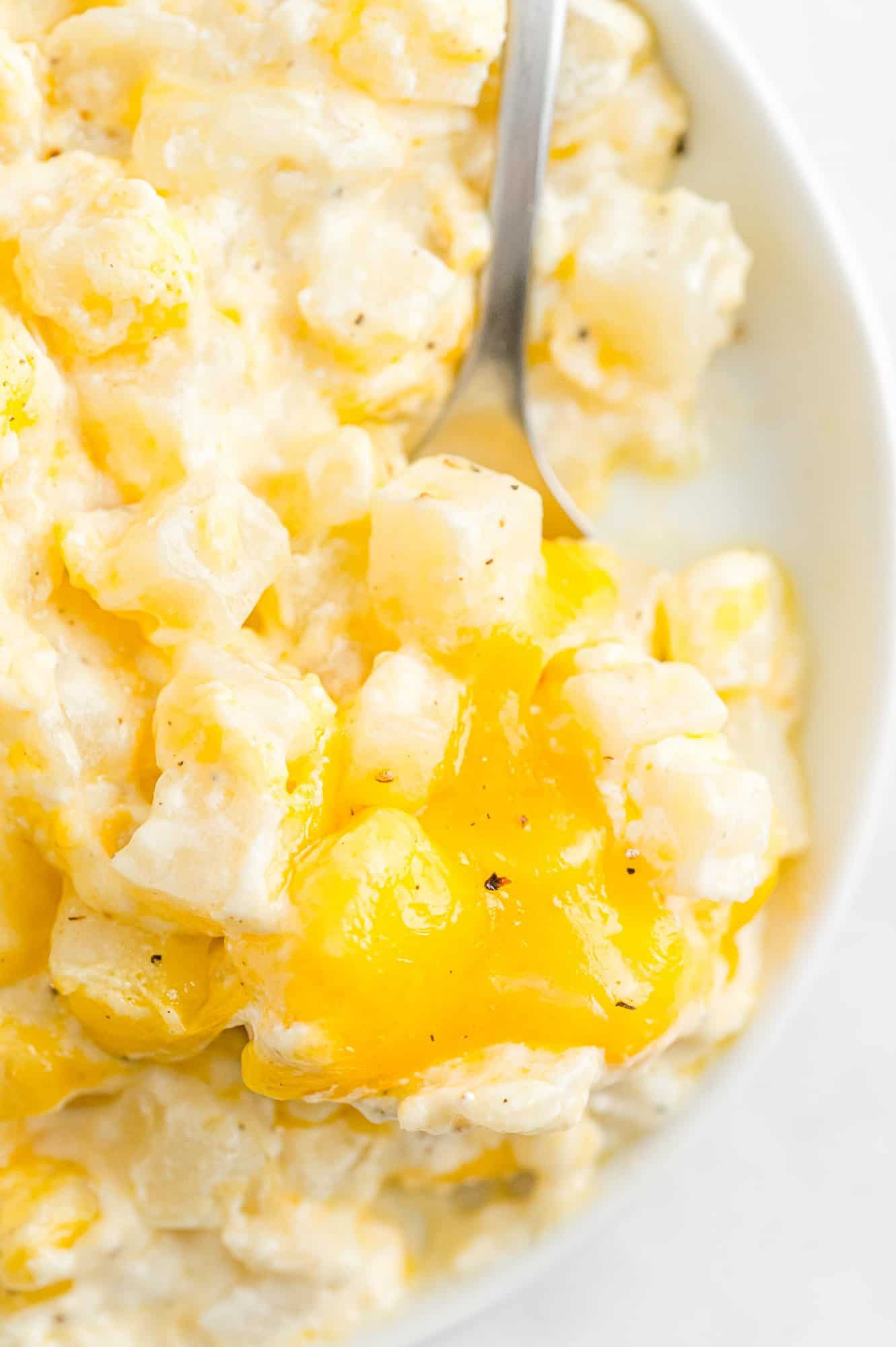 Slow cooker cheesy potatoes being scooped with a silver spoon.