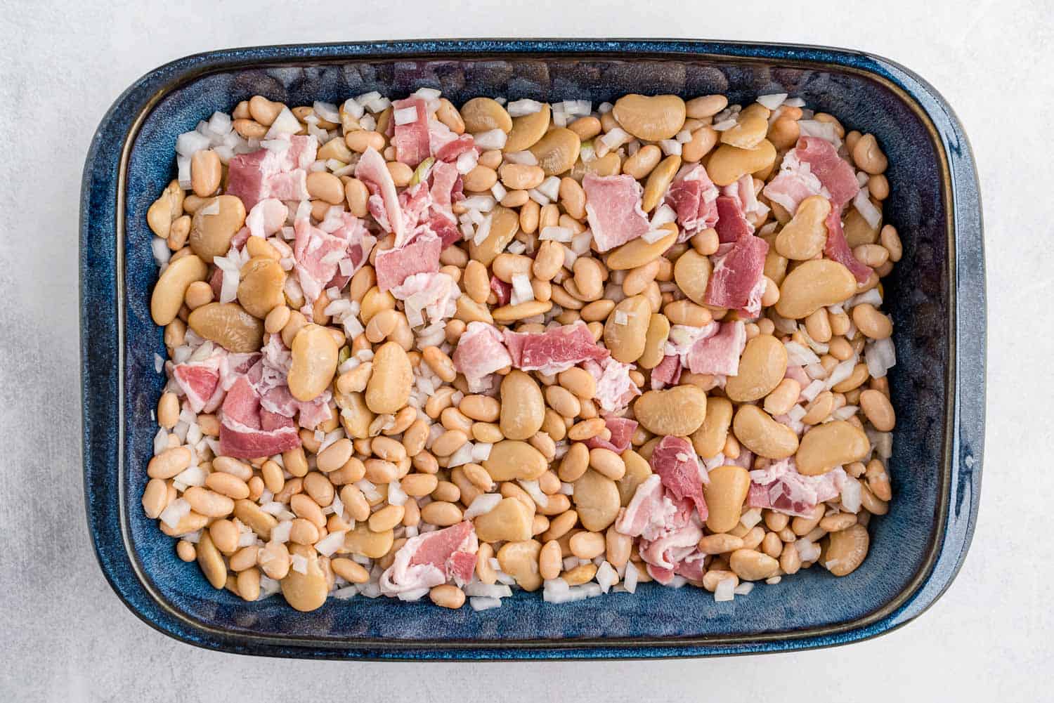 Beans, uncooked bacon, and onions in a baking dish.