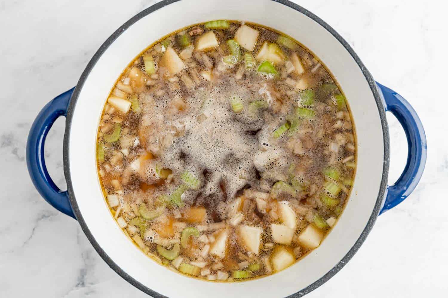 Beef and potatoes in broth, in a blue dutch oven.