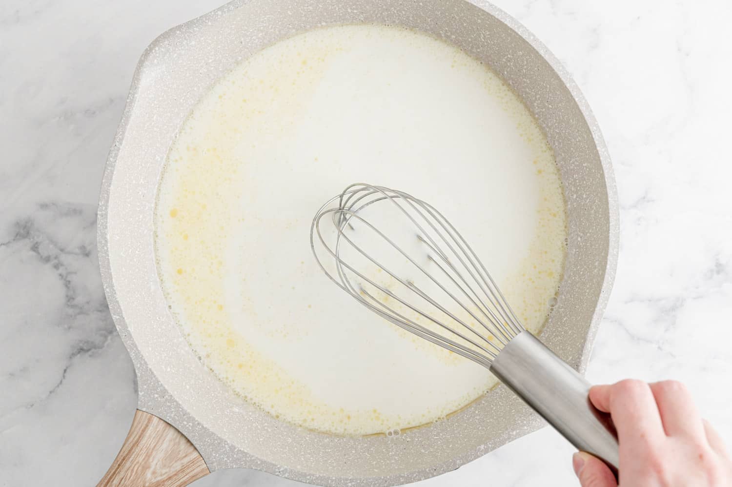 White sauce in a white saucepan, a whisk about to go into it.