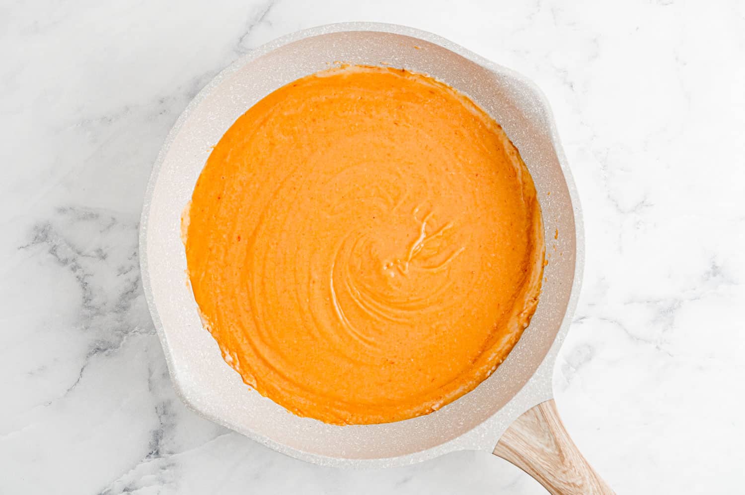 Bright orange sauce in a white saucepan.