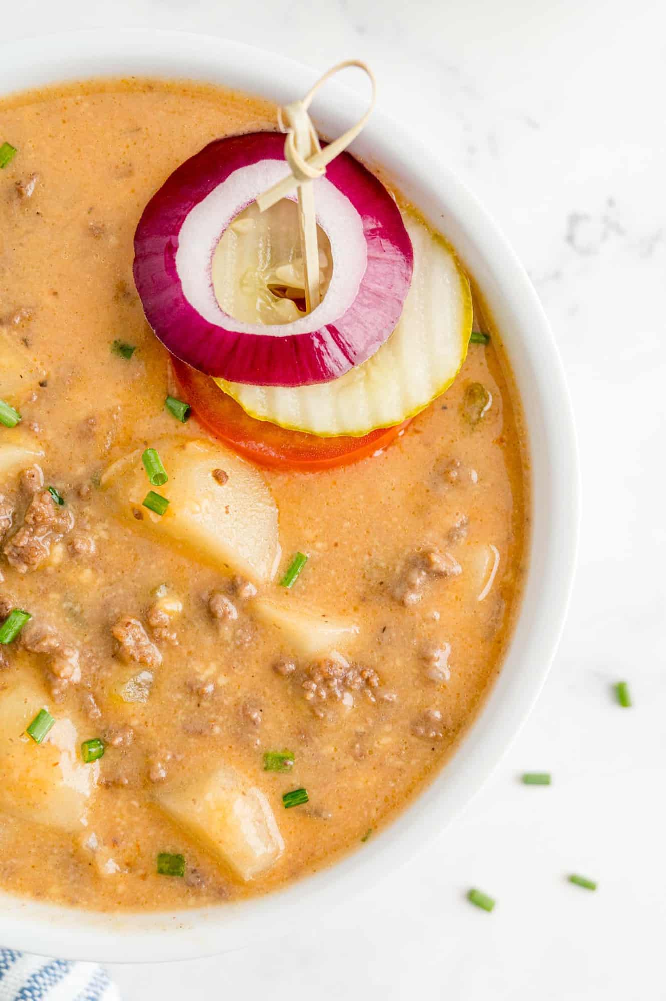 Close up of cheeseburger soup with burger toppings (onion, pickle, tomato).