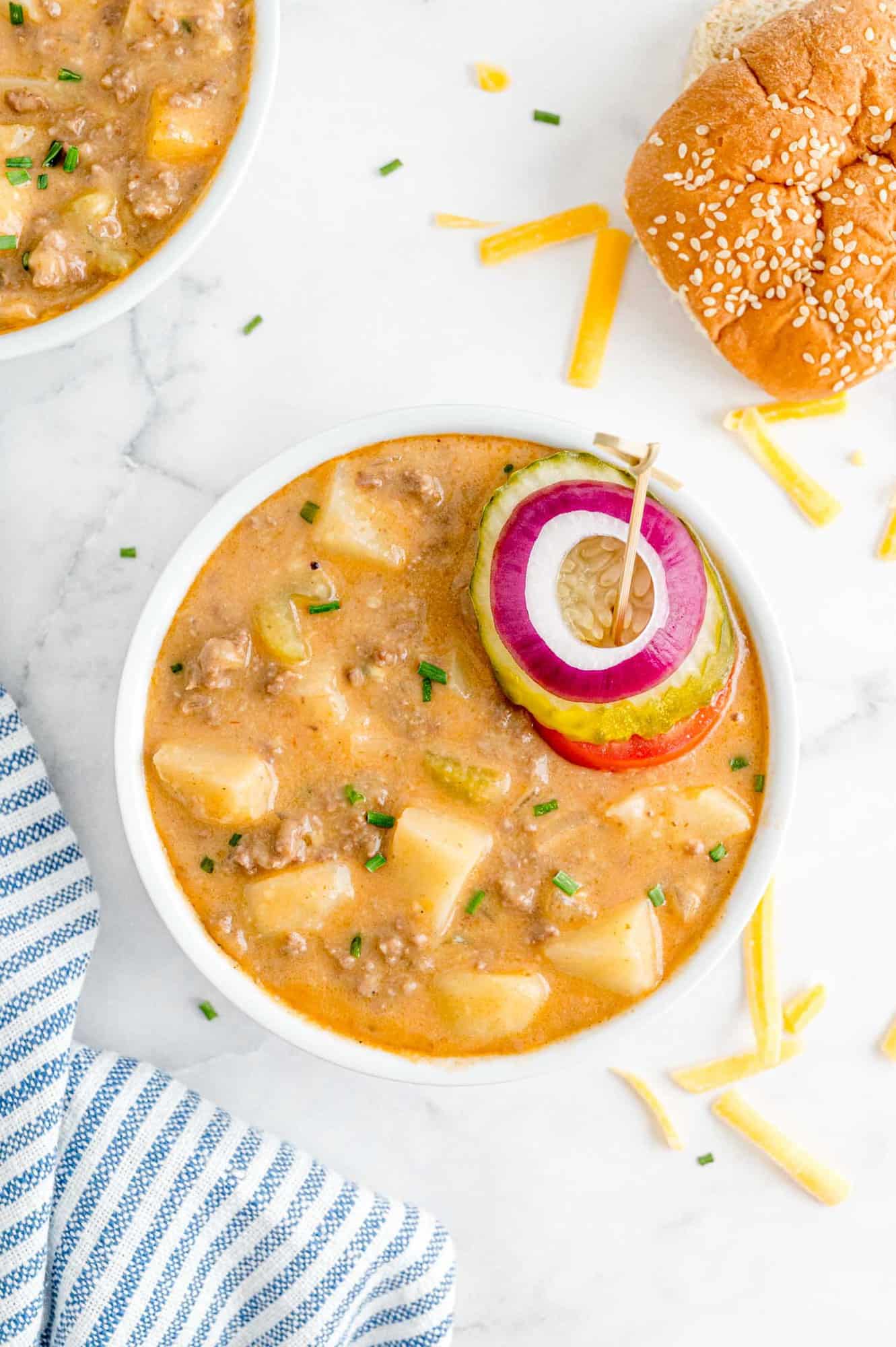 White round bowl of cheeseburger soup topped with onion, pickle, tomato.