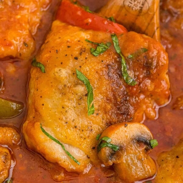 Cooked chicken thigh on a spoon with tomato sauce and a mushroom.