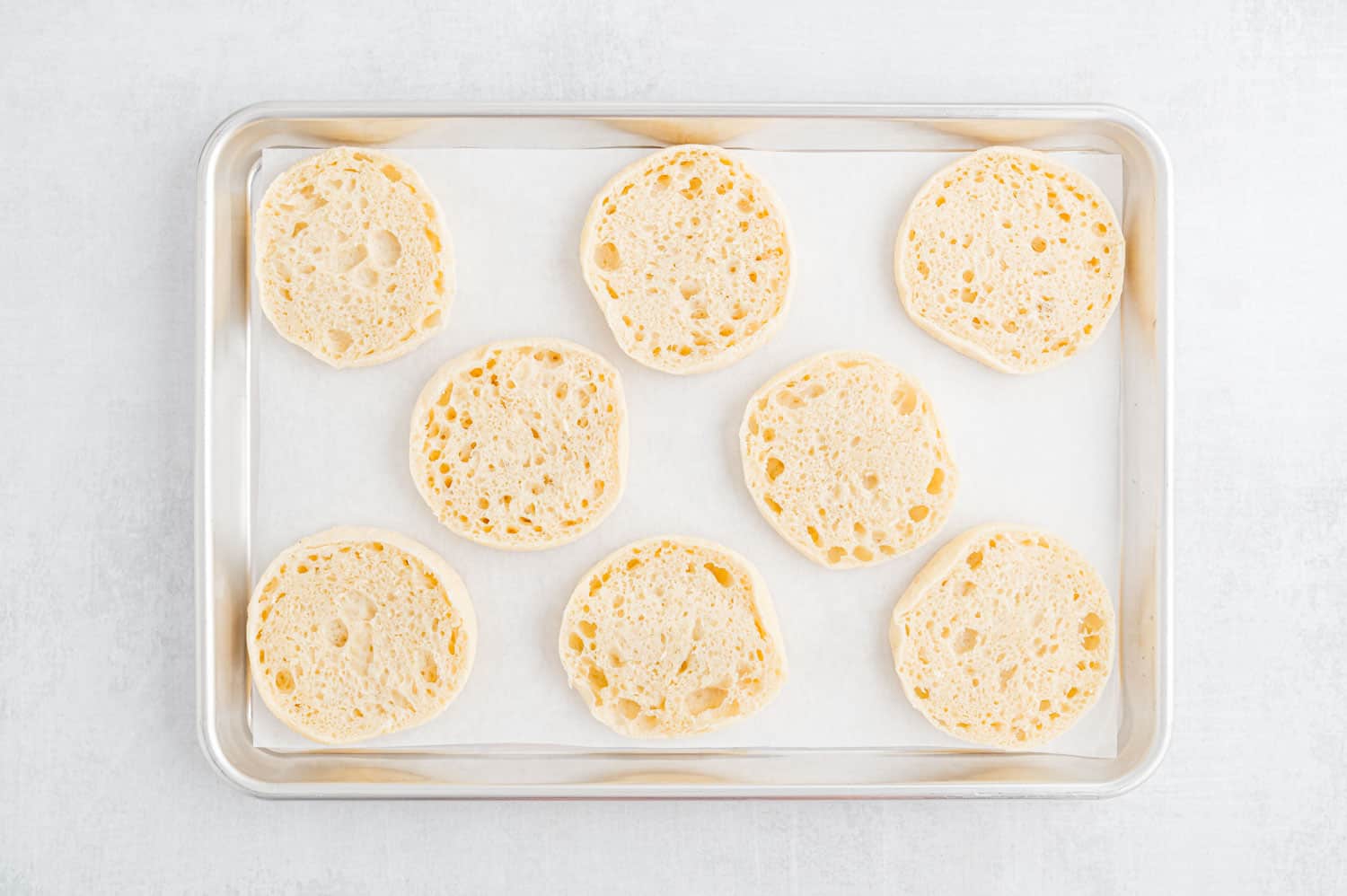 English muffins cut in half, on a sheet pan.