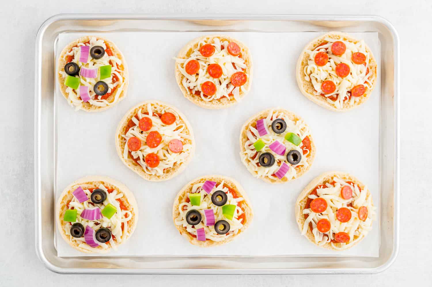 Uncooked english muffin pizzas on a sheet pan.