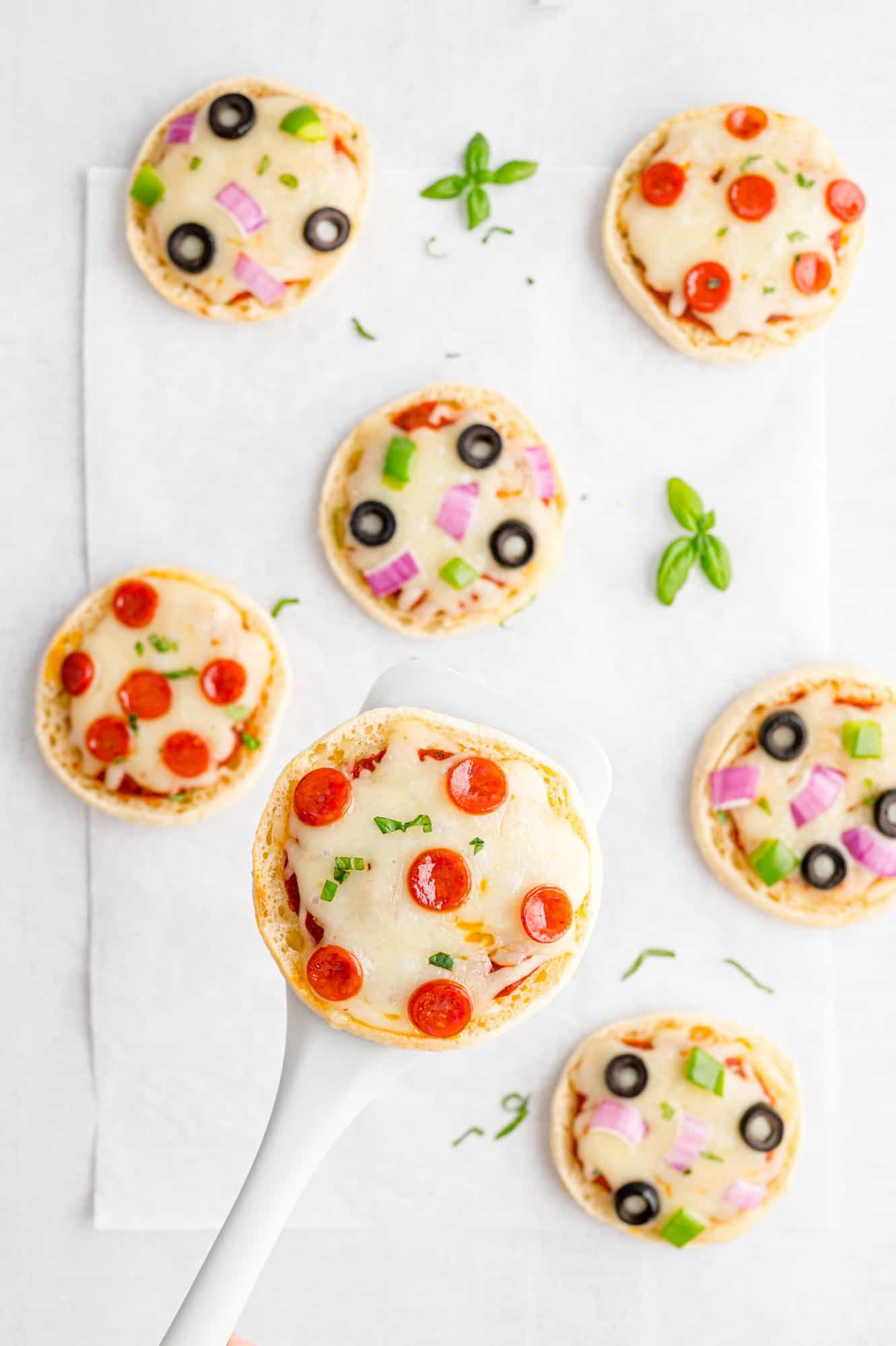 English muffin pizza on a spatula, others visible on a sheet pan.