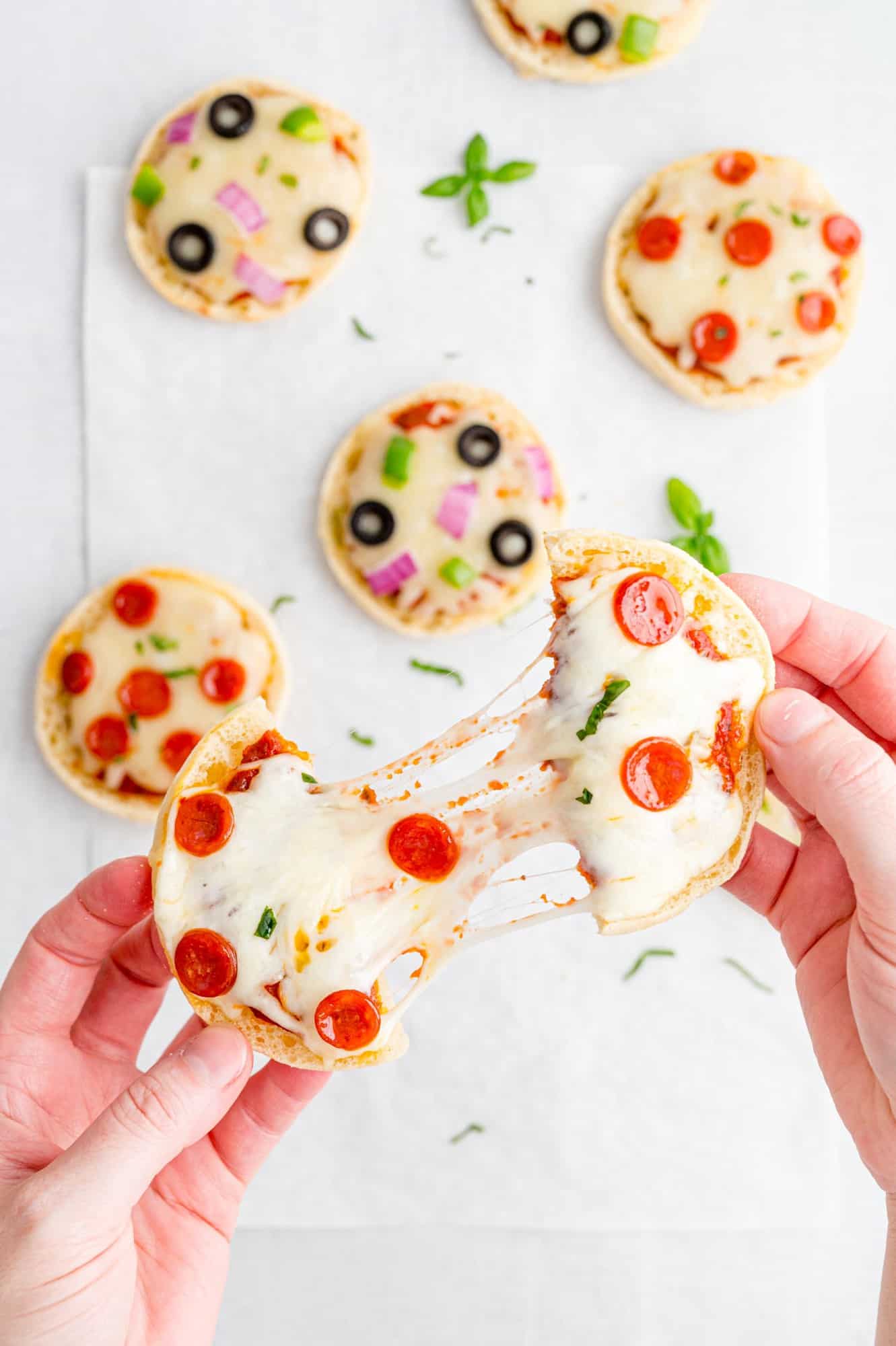 Two halves of an english muffin pizza being pulled apart, connected by cheese.