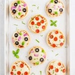 Overhead view of english muffin pizzas on a parchment paper lined baking sheet.