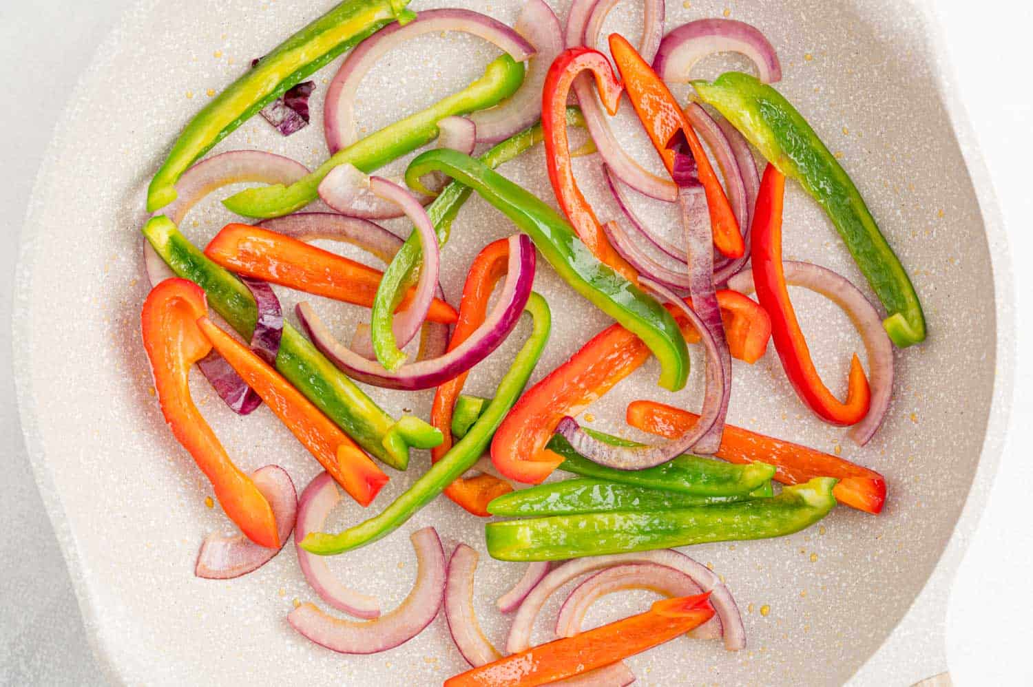 Sautéed peppers and onions in a white frying pan.