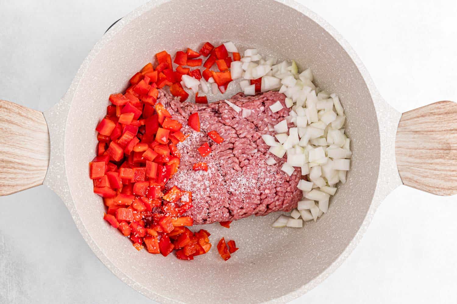 Uncooked beef, peppers, and onions in a white pan.