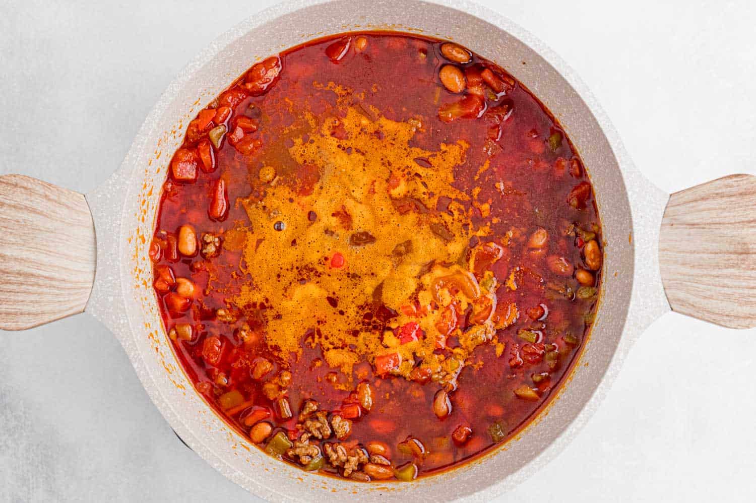 Chili simmering in a white pan with wooden handles.