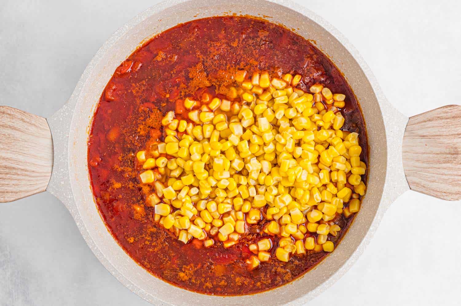 Corn sitting on top of a pot of chili, not yet stirred in.