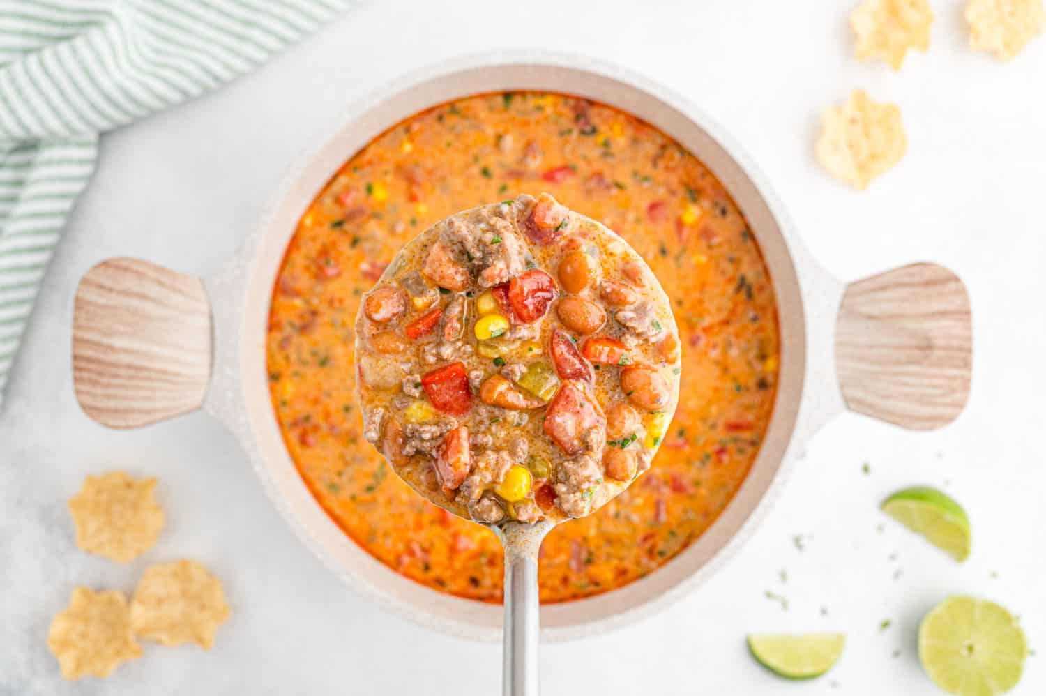 Ladle of creamy queso chili over a pan of more chili.