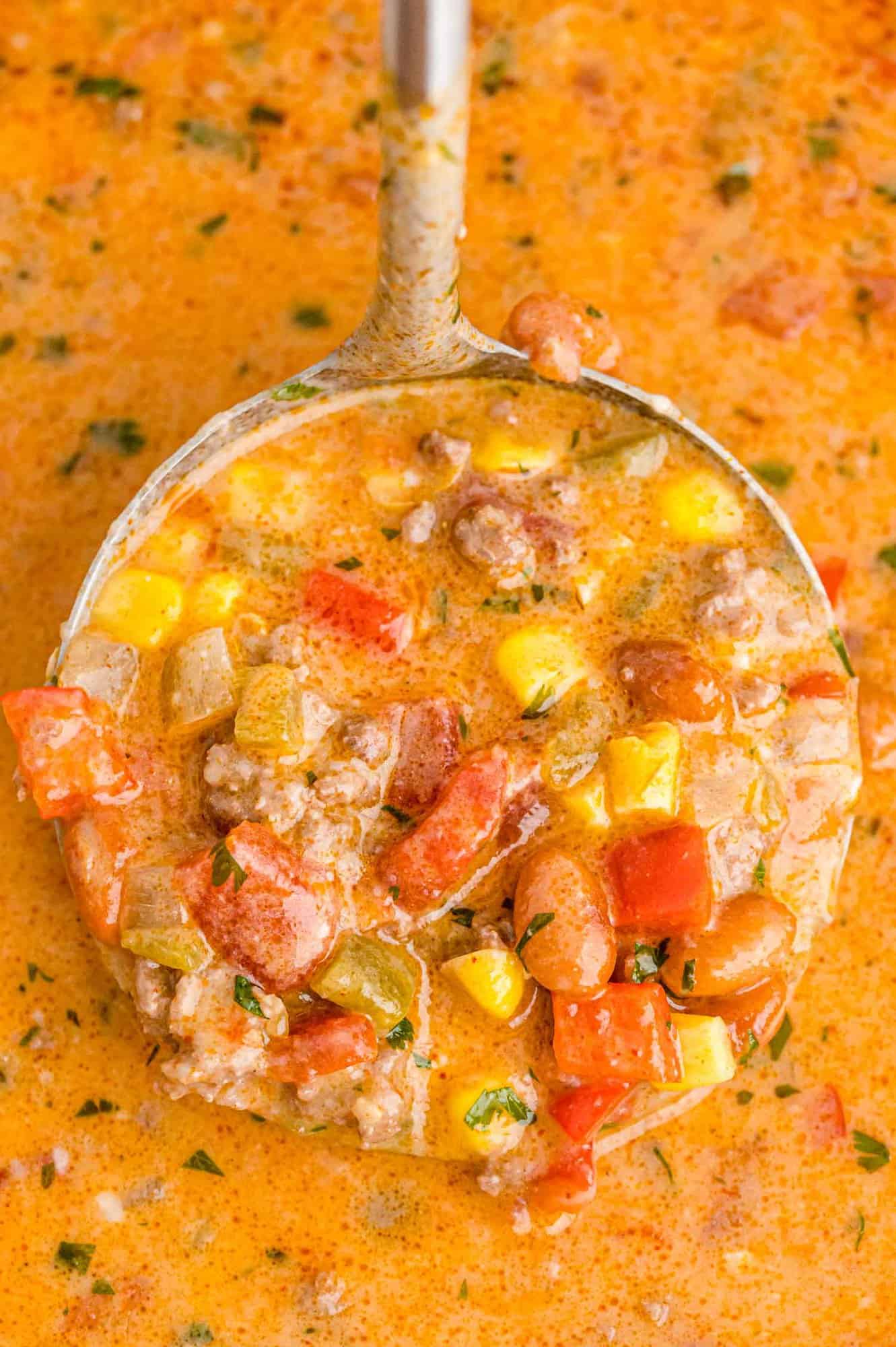 Creamy chili on a ladle, showing beans, red peppers, corn and more.
